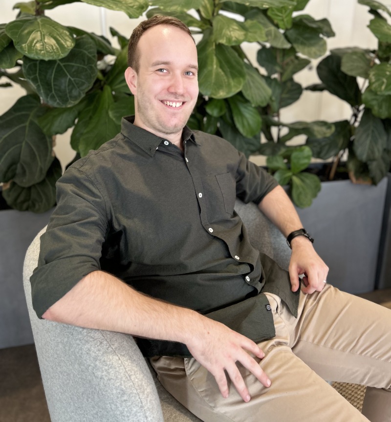 Man sitting casually on a couch in front of plants smiling