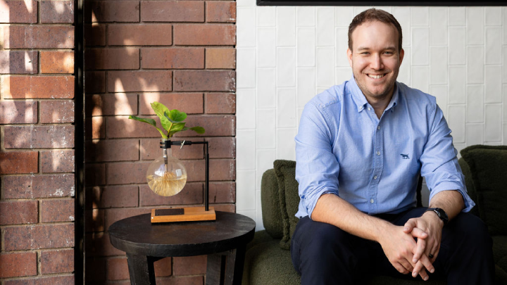 Jonathon Shipton sitting on couch hands together smiling at camera